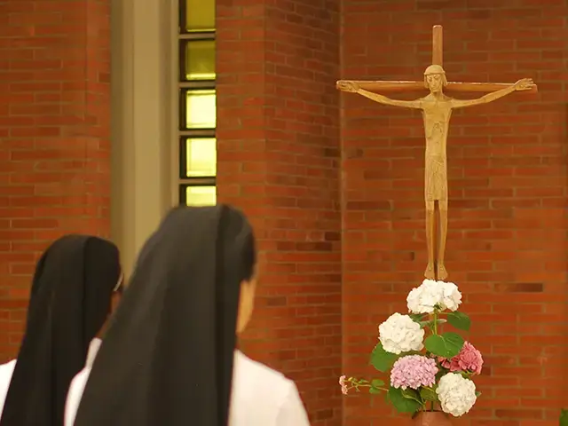 Sisters kneeling before crucifix and flowers
